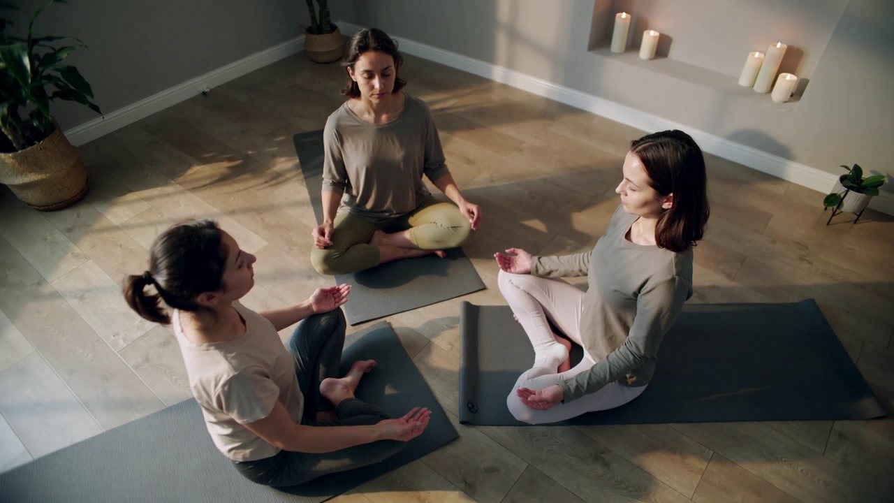 Kvinde guider til langsomme åndedræt i oplyst meditationsstudie, med yogamåtter og leggings.