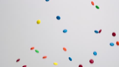 bright multi colored chocolate covered candies falling in slow motion on white backdrop