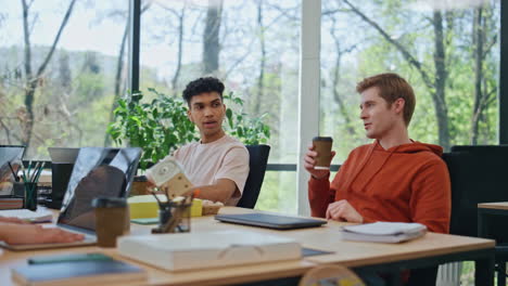 young man finish laptop work shutting notebook lid at office. coworkers talking