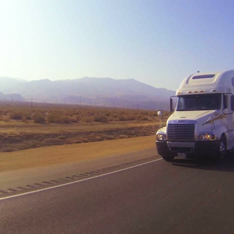 un camión de transporte de automóviles se mueve por el desierto en esta toma de punto de vista