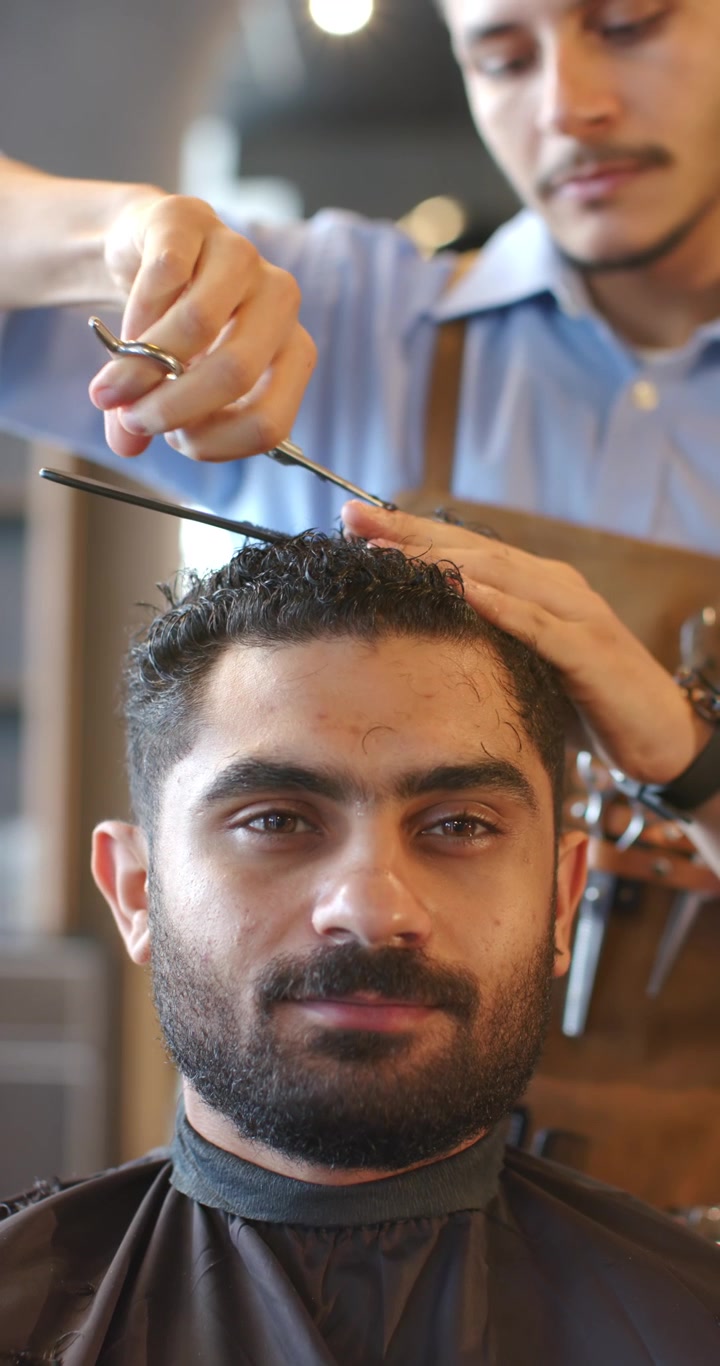 Vertikal video: Afrikansk barber og mandlig kunde, barberen placerer kam og saks, former krøller i salonen.