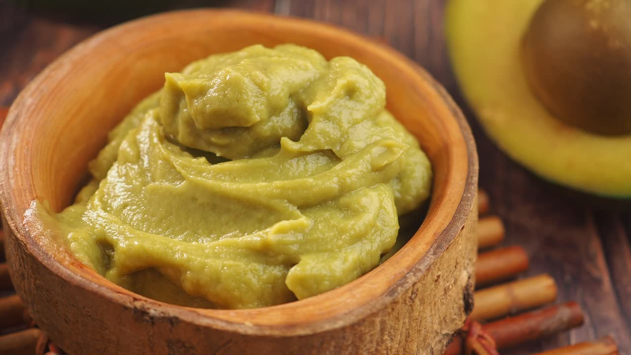 Fresh Guacamole in a Wooden Bowl with Halved Avocado