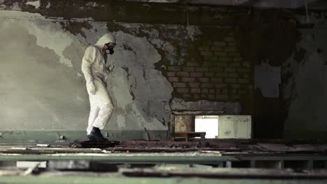 worker in protection suit standing against destroyed brick wall in abandoned building