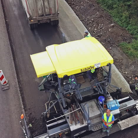 a truck with bitumen slowly drives up to a paver on a highway near a forest landing on the background of road repair works near the city. aerial view.