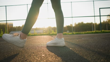 low angle view of athlete bouncing volleyball, stepping forward with sunlight creating a golden glow on the ground, preparing for a serve or play during volleyball practice in outdoor court