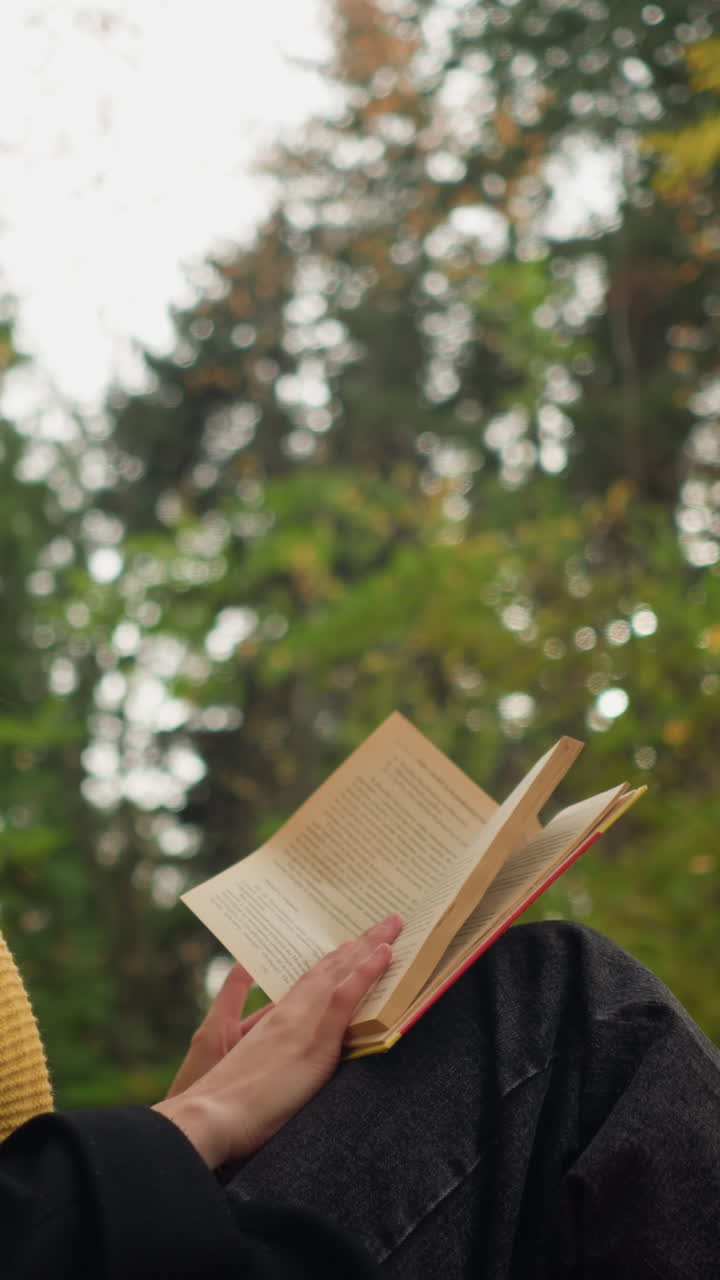estudiante universitario se sienta en soledad apoyado en un árbol, profundamente involucrado en el libro, volviendo páginas pensativamente en un entorno al aire libre pacífico rodeado de hojas de otoño y la belleza de la naturaleza