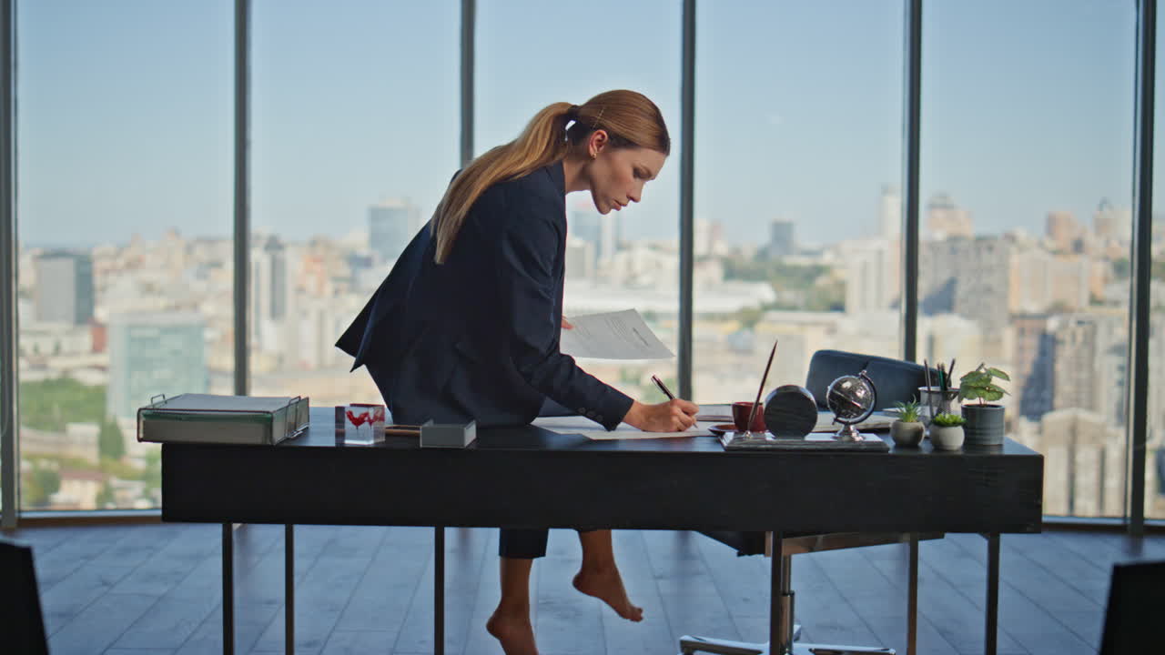 Donna d'ufficio che lavora a piedi nudi alla finestra panoramica. Manager concentrata che esamina documenti.