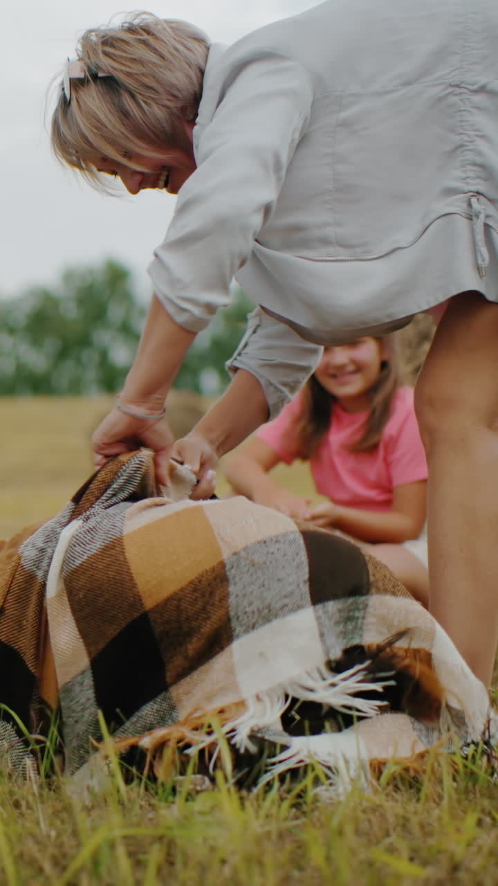 momento alegre como perro juguetón cubierto con una manta, el dueño se ríe mientras lo abre, la hija se agacha cerca disfrutando de la escena divertida, ambiente al aire libre cálido con balas de heno, ambiente de campo