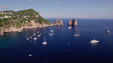 a 4k aerial of boats and private charter yachts in the sea around the famous faraglioni rocks of capri, a famous island that is a popular luxury vacation destination in italy along the amalfi coast