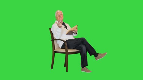 white-haired senior man reading a book to camera on a green screen, chroma key