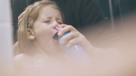 woman irrigates nose of sick girl with nasal spray at mirror