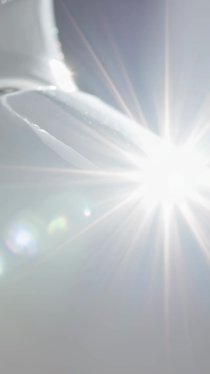 Video verticale: Telecamera che si inclina mostrando il sole che crea bagliori a stella che si muovono nel cielo sopra una curva bianca