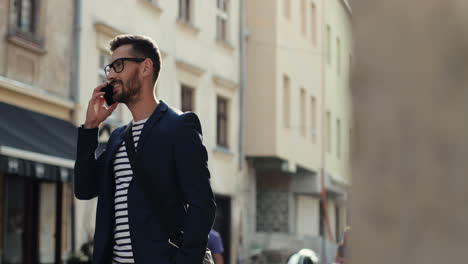 stylish man standing in the old town street in sunlight and talking on the mobile phone