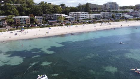 Drone-flying-towards-a-beach,-boats-below-and-a-beach-town-in-the-background