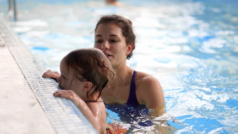 Beautiful mother teaching cute baby girl how to swim in a swimming pool. Child having fun in water with mom.