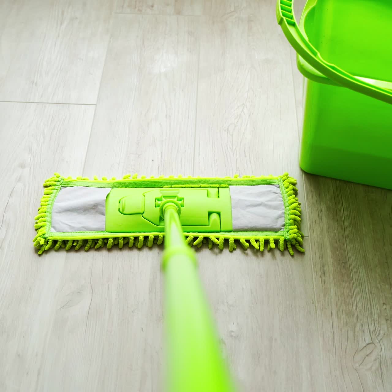Cleaning floor with water and swab. Green mop moving on the parquet floor near the green bucket with water. Daily household routine. Hygiene concept.