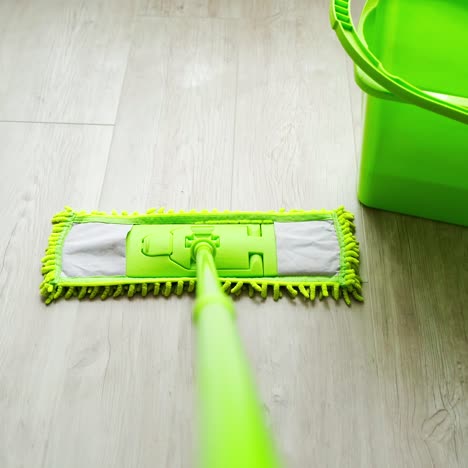 cleaning floor with water and swab. green mop moving on the parquet floor near the green bucket with water. daily household routine. hygiene concept.