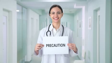 Happy-Indian-female-doctor-holding-PRECAUTION-banner