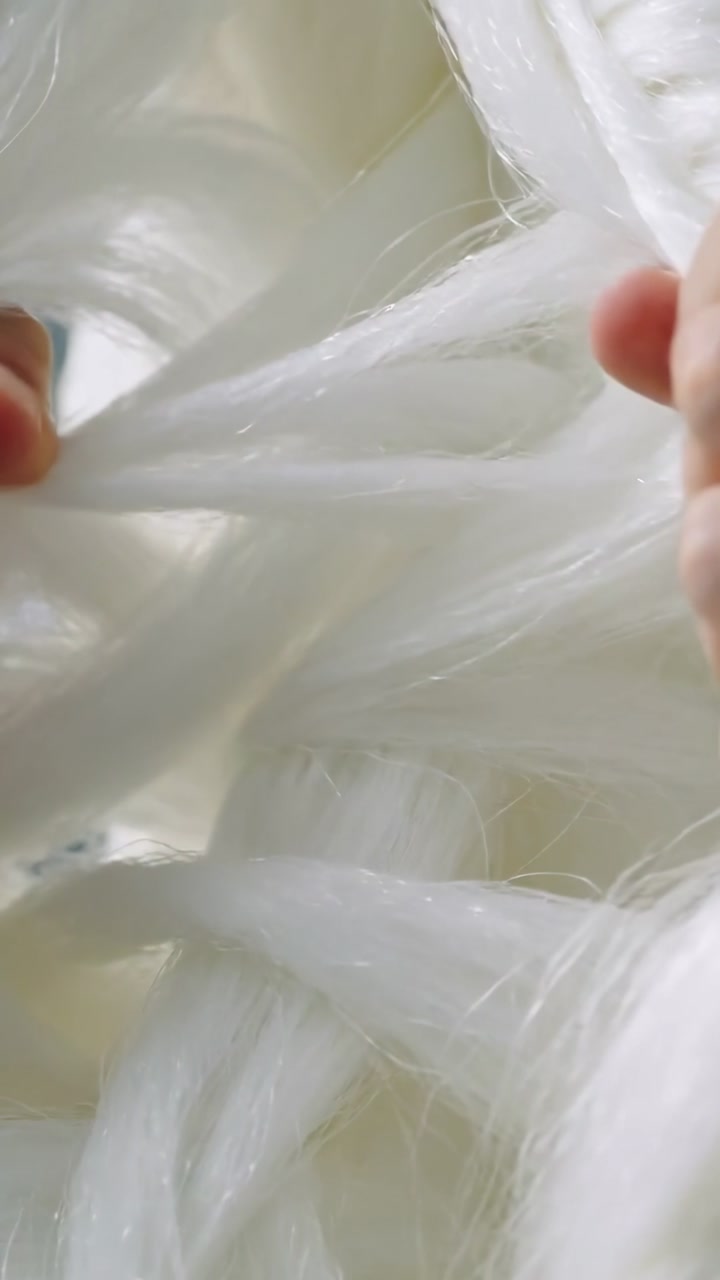 Vertical video: Entering hands pulling white fibers on pale mat, fluffing strands and showing ring
