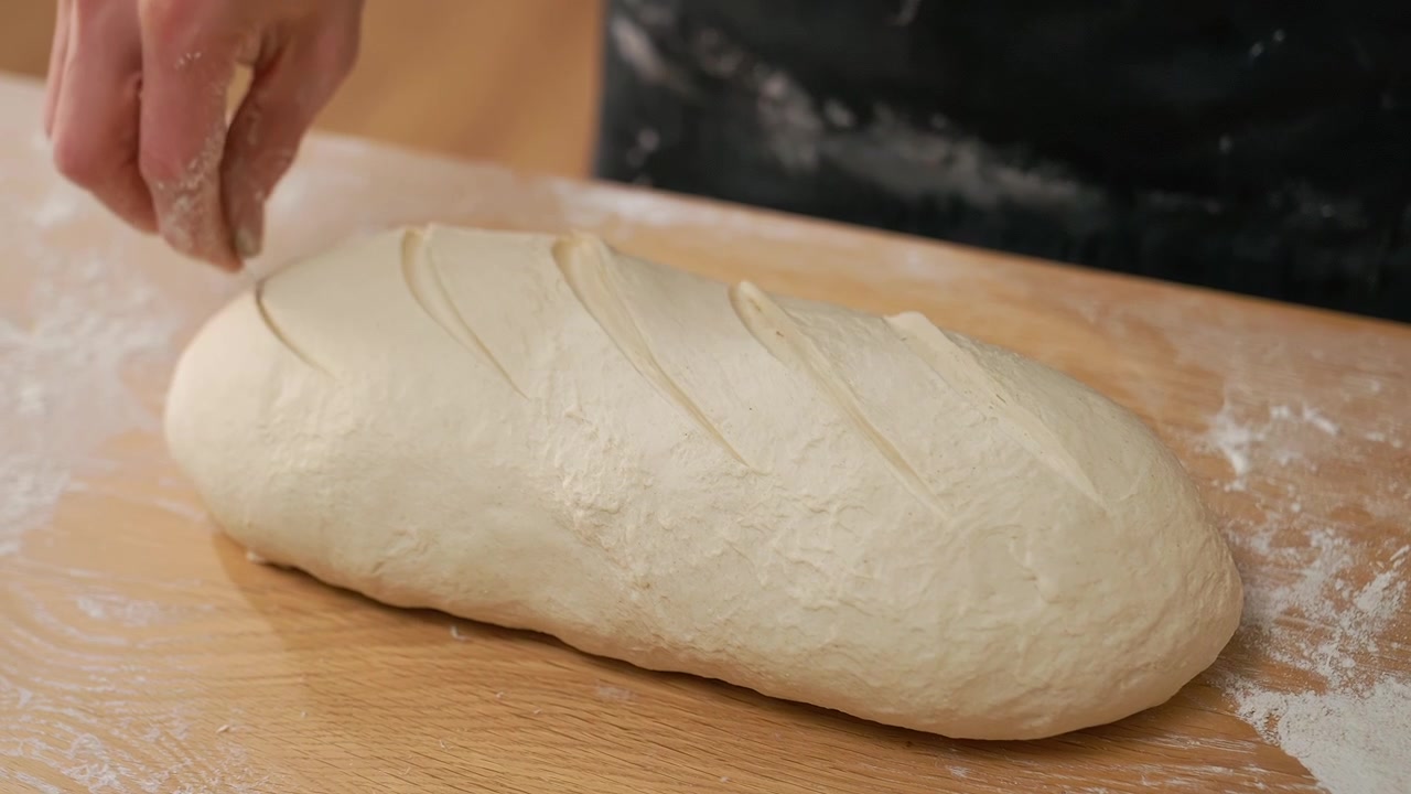 Primo piano di una mano che incide l'impasto di pane crudo su un tavolo di legno