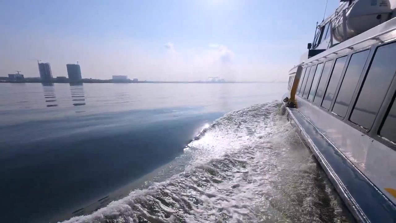 Echtzeit-Seitenansicht mit 60 Bildern pro Sekunde einer Fähre, die die ruhigen Gewässer der Straße von Singapur überquert, mit einer sichtbaren fernen Stadtsilhouette.