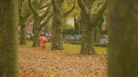 Mujer-Joven-Corre-En-El-Parque-Con-Hojas-Caídas-En-Otoño