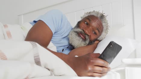 senior man using smartphone while laying on bed at home