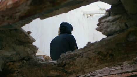 young man, teenager, sitting high on a beam in an abandoned house puts on his hood