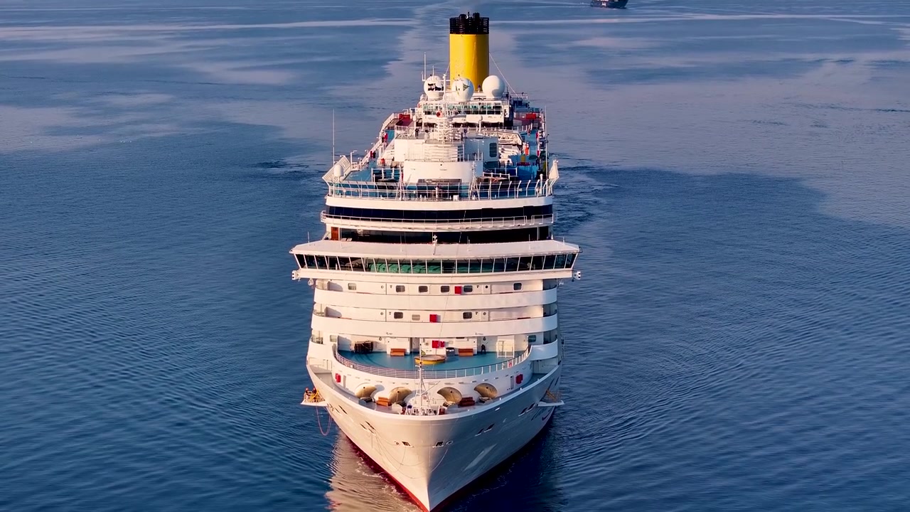 Imponerende luksuskrydstogtskib navigerer gennem rolige blå havvande. Majestætisk luftperspektiv fanger skibets rejse til søs