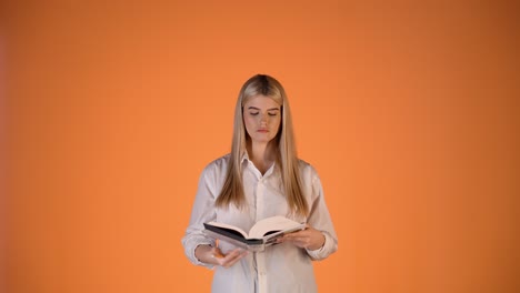 joven rubia concentrada en serio leyendo un libro y volviendo páginas, colorida toma de estudio