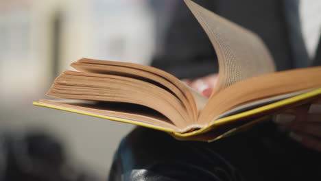 close-up of book pages being flipped by a hand adorned with a ring and polished nails, dressed in black clothing, the background is blurred