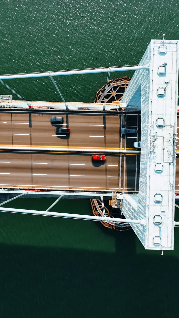 Footage above the support of high suspension bridge. Transport moves quickly by the highway on the bridge. Sunny day top view.