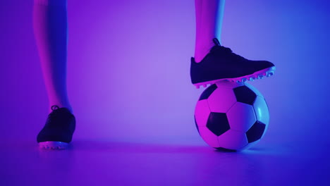 Close-up-of-the-foot-of-a-professional-black-football-player-standing-on-the-ball-in-slow-motion-in-the-blue-red-neon-light-of-the-studio.-Brazilian-football-player-foot-on-the-ball-to-pose
