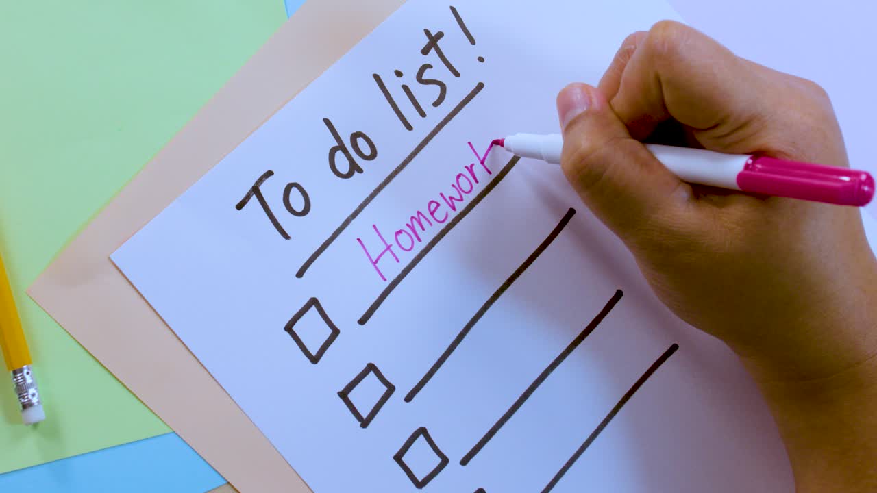 Person writes 'Homework' on checklist paper in bright, overhead lighting with stationary pencil nearby
