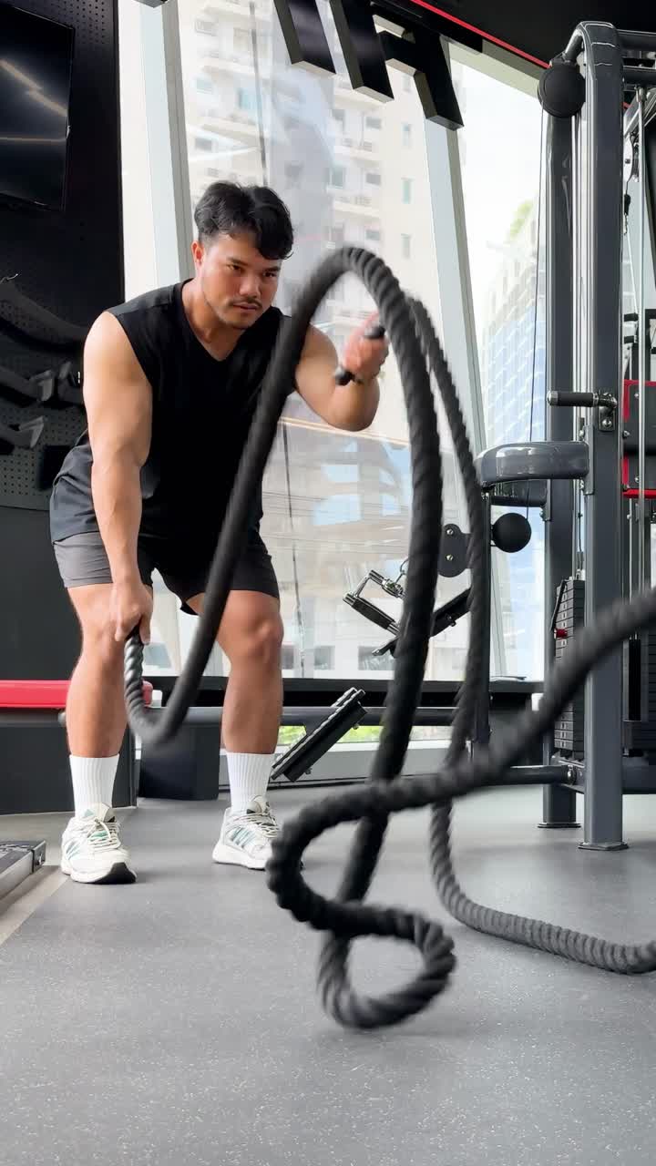 Un hombre se ejercita vigorosamente con cuerdas de batalla en un gimnasio bien iluminado, mostrando fuerza y determinación.