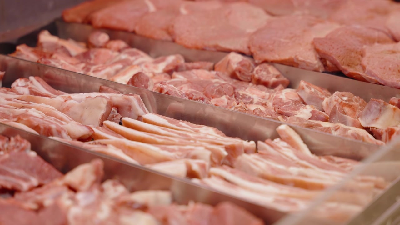 Assorted raw pork strips and steaks lie in separate sections of a chilled butcher case, ready for customer selection or food industry use.