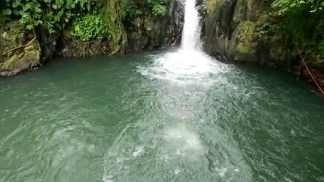 Un-Joven-Adulto-En-El-Acantilado-De-La-Cascada-Kroya-Salta-Sin-Miedo-Desde-Una-Plataforma-De-Buceo-De-Cabeza-Hacia-Una-Piscina-Natural-En-Medio-De-Exuberantes-Paredes-Rocosas-Y-El-Bosque-De-Aling-Aling,-Bali