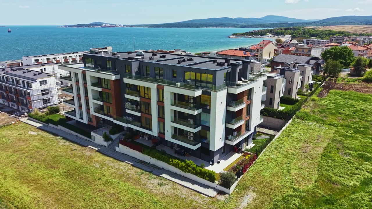 Edificio moderno vicino al mare con erba verde e acqua blu sullo sfondo in una giornata di sole che mostra una scena di città costiera.