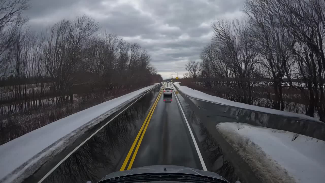 Dashcam video captures a straight road flanked by snowy fields under a cloudy sky