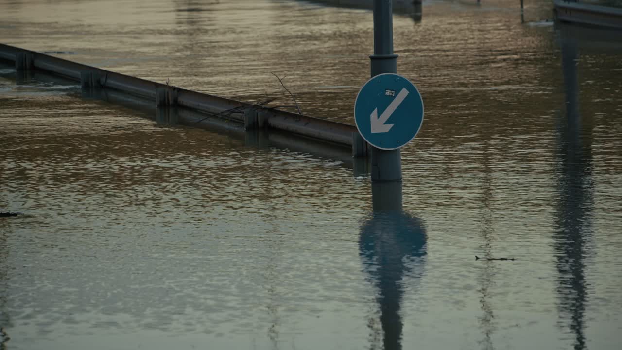 Submerged traffic sign with a blue arrow pointing downwards, surrounded by floodwater during Budapest Flood 2024