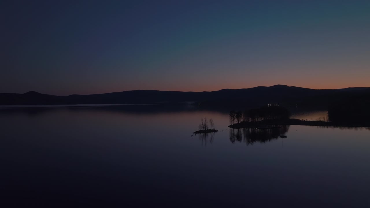 Ilmakuvaa Turgoyak-järvestä hämärässä, jossa on pieni metsäinen saari, tyyni heijastava vesi ja tumma vuorisiluetti, rauhallinen luonnonmaisema Tšeljabinskin alueella Venäjällä