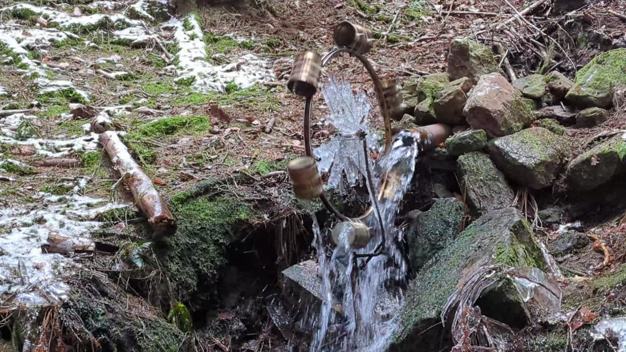 산 아래로 흐르는 작은 개울에 의해 구동되는 윈터리 삼림 지대에 금속 캔이 부착된 수제 나무 방앗간