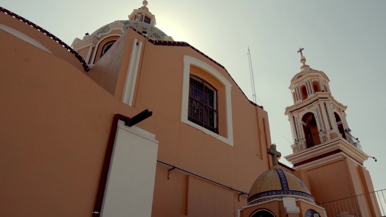 Vista dal basso di una chiesa con cupole e campanile, luce solare che brilla dietro la struttura, facciata calda e dettagli architettonici, edificio storico a Cholula Puebla ripreso alla luce del giorno.
