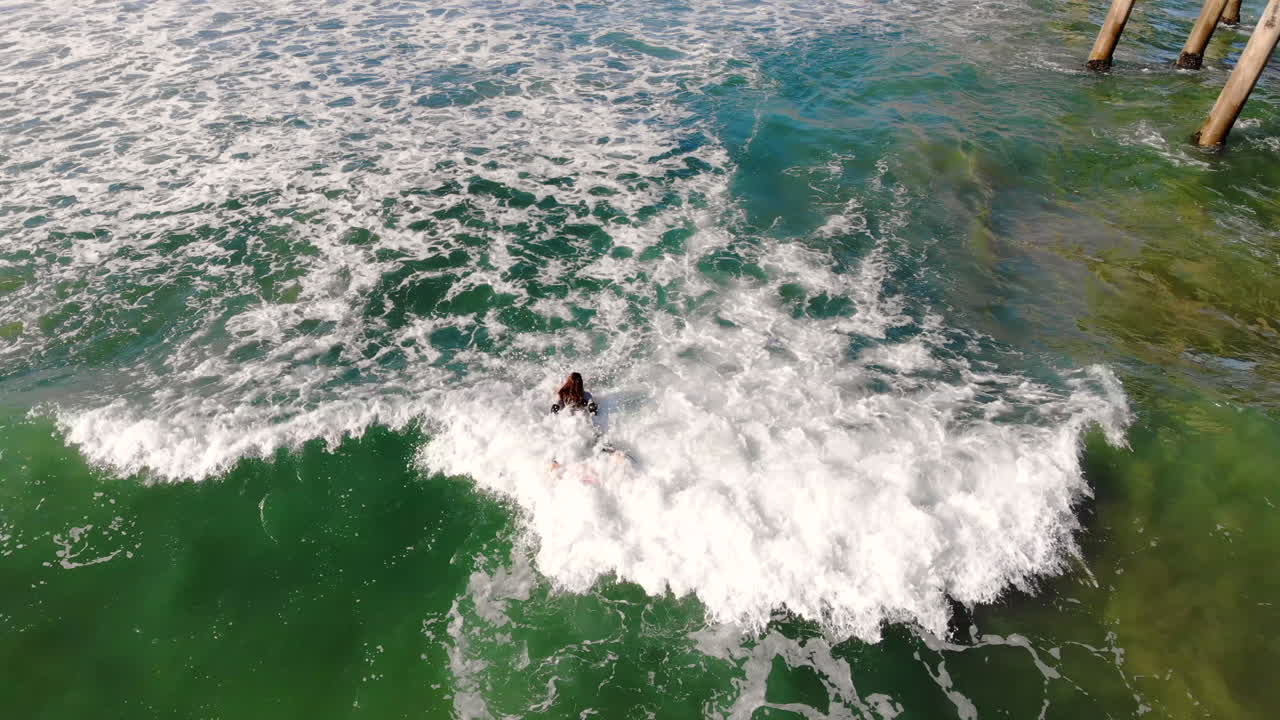 공중 4k 무인 항공기, 이른 아침, 태평양, 긴 서핑 보드와 함께 헌팅턴 비치 부두에서 파도 속으로 노를 젓는 여성 서퍼 소녀 조 스나이더에게 기울어져 멋진 비행