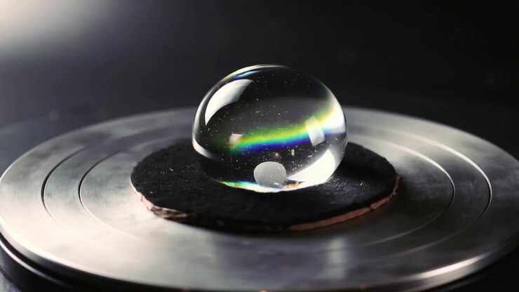 Reacting clear spherical bead shifting color band on pad atop metal platter on bench