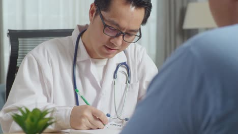 close up of asian male doctor writing prescription, laughing and talking to a fat male patient in clinic