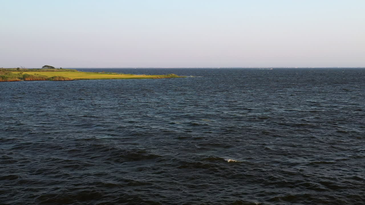 이스트 아이슬립 정박지의 물 위를 꾸준히 맴돌고 있는 낮은 공중 드론 샷 - 일몰 시 습지 지역이 보이는 공원