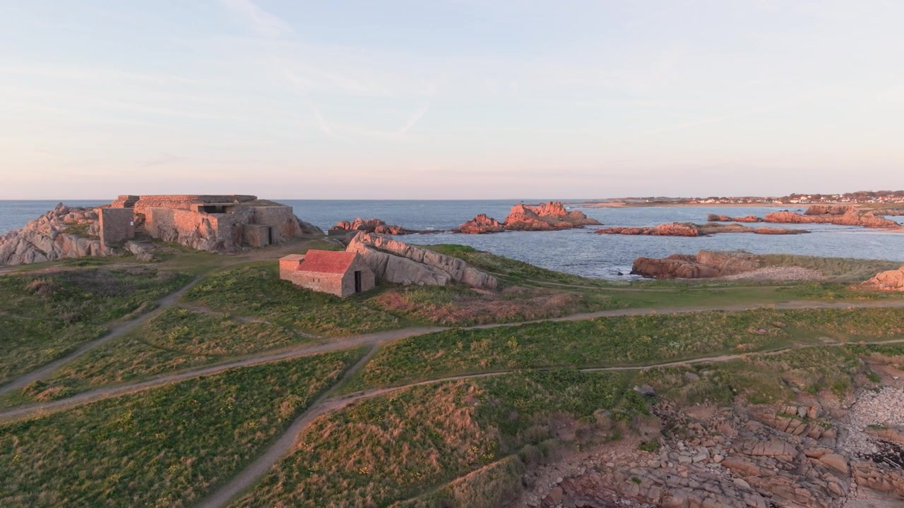 Guernsey, Kanaløerne, Vestkysten. Panorerende droneoptagelse af gammelt militærfort på toppen af en klippefyldt odde med barsk kystlinje og bugt bagved i den sene eftermiddags gyldne sol med roligt hav