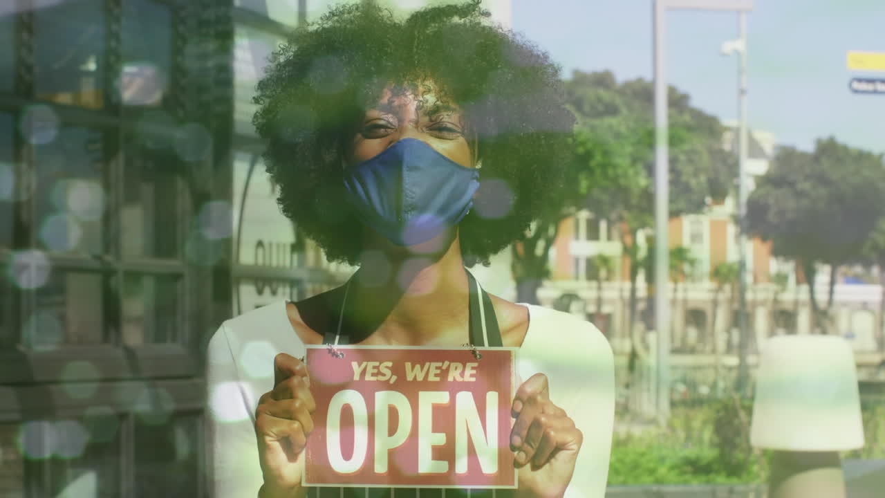 Punti luce su sfondo di cameriera afroamericana con mascherina che tiene in mano un cartello 'aperto'