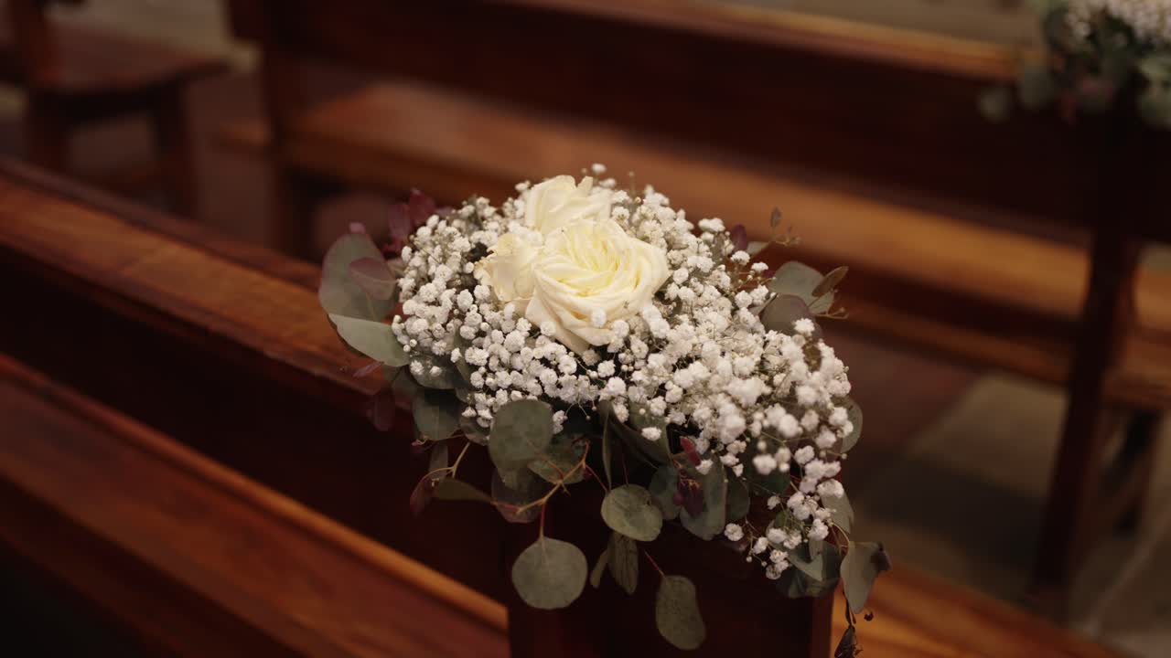 wedding floral arrangement with white roses and baby’s breath on church bench